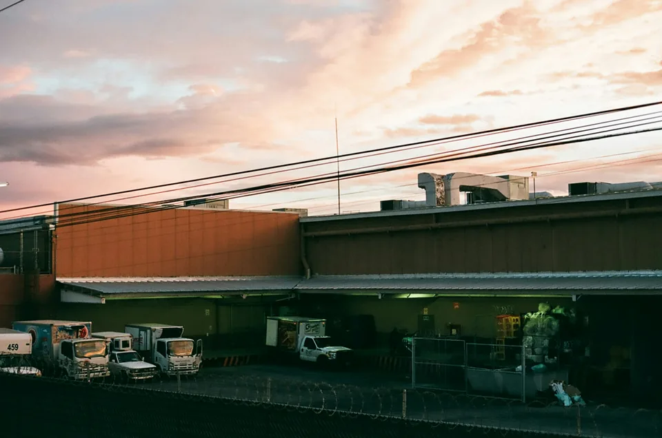 Box trucks backed up to a warehouse dock at first light, under a pink sky.