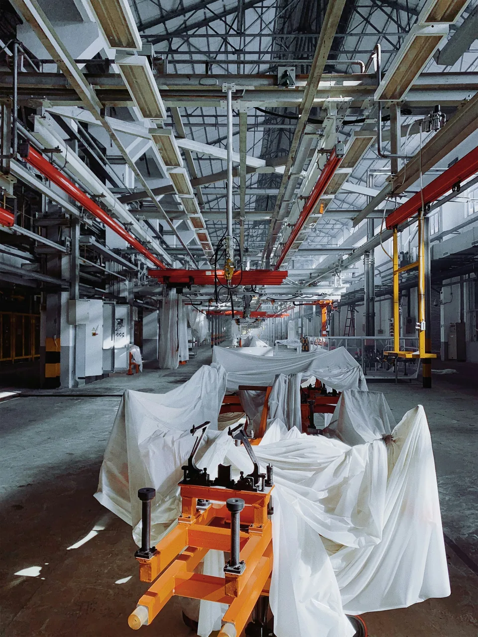 A new overhead assembly line in a large plant, every station still draped in white dust sheets, an orange jig at the front.
