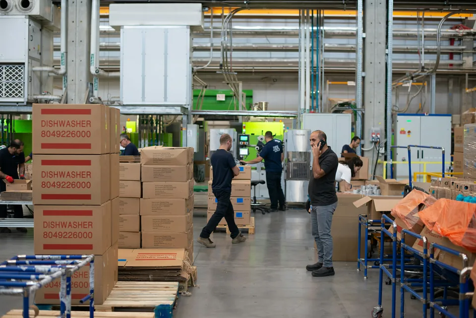 A man on the phone stands in the middle of a busy plant floor while the crew around him stacks cartons and works the lines.